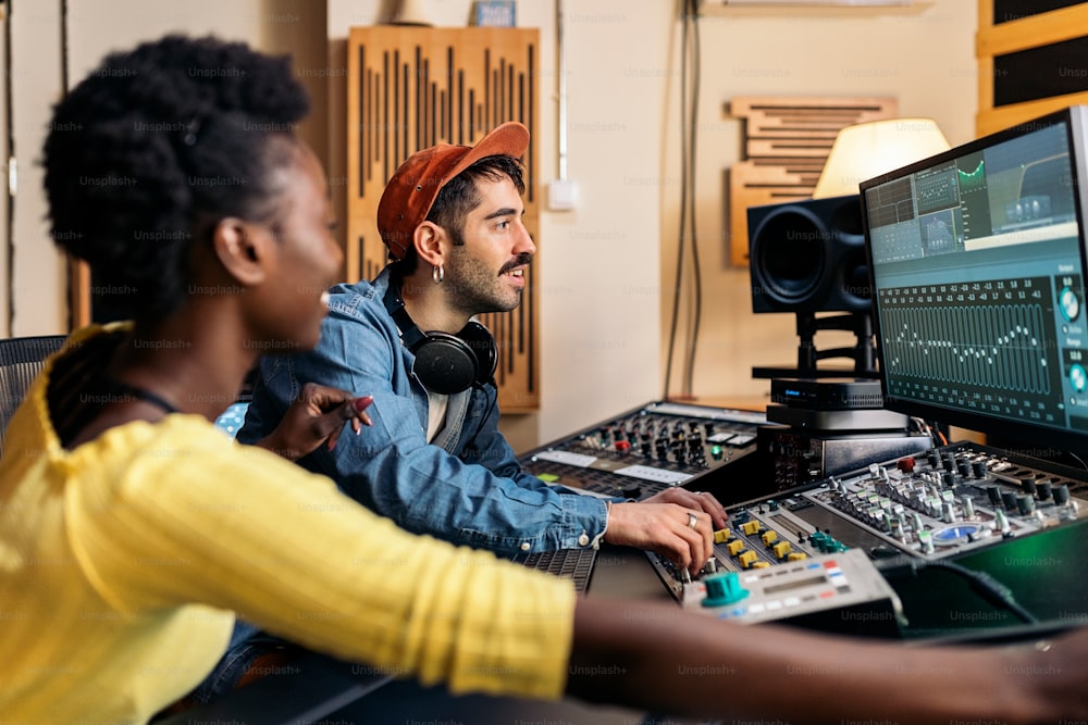 Foto de banco de imagens do cantor negro feliz que trabalha no estúdio de música profissional com o produtor musical jovem.