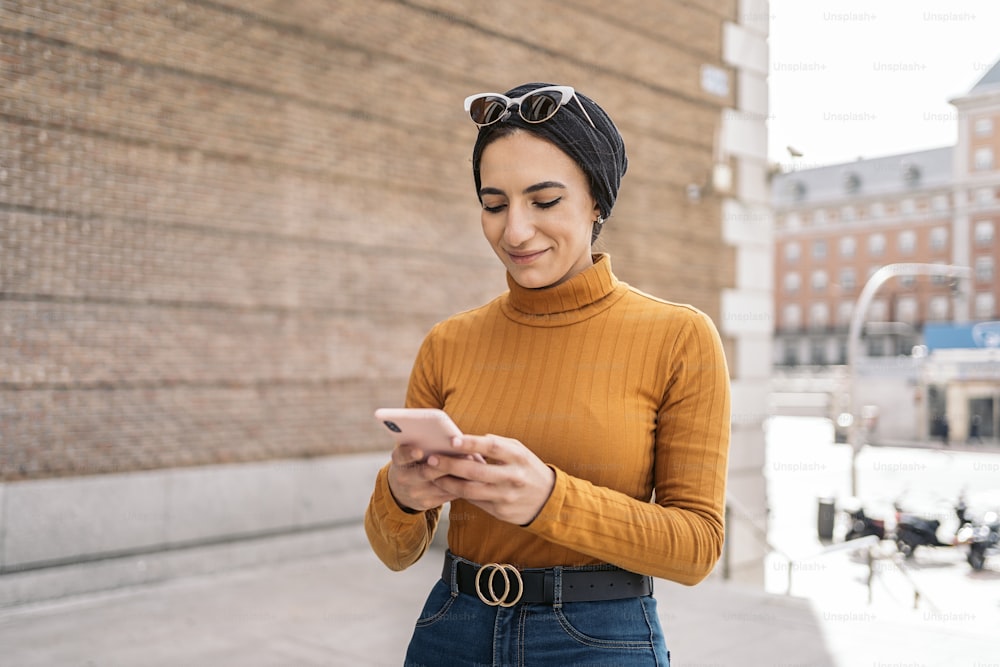 Pretty young muslim woman wearing head scarf using her mobile phone in the street.