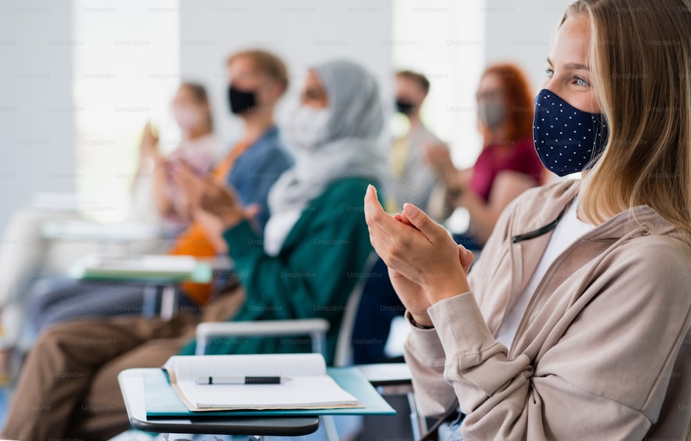 Happy university students clapping in classroom indoors, coronavirus and back to normal concept.