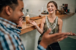 Beautiful generation z girl laughing at bar counter of a trendy coffee shop being expressive with mixed race guy