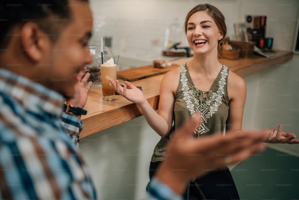Beautiful generation z girl laughing at bar counter of a trendy coffee shop being expressive with mixed race guy