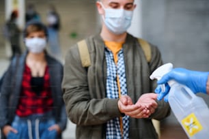 Giovani studenti con maschere per il viso di nuovo al college o all'università, coronavirus e concetto di disinfettare le mani.