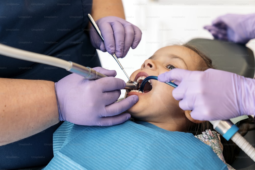Foto de banco de imagens da menina bonita durante a revisão no dentista. Ela está de boca aberta.