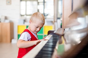 A cheerful down-syndrome school boy sitting at school, playing piano.