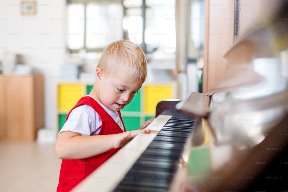 Un alegre escolar con síndrome de down sentado en la escuela, tocando el piano.