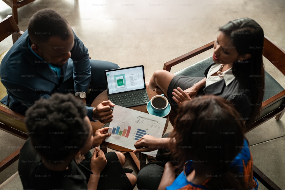 Un grupo de jóvenes empresarios africanos revisan gráficos y papeleo durante una reunión mientras toman un café en una mesa en una oficina moderna