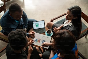 Groupe ciblé de jeunes hommes d’affaires africains en train de parcourir des graphiques et de la paperasse lors d’une réunion autour d’un café à une table dans un bureau moderne