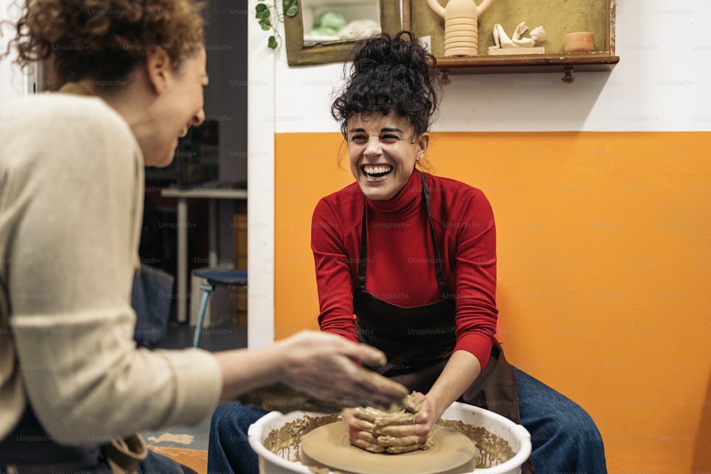 Stock photo of happy women in apron working behind a potter's wheel in a workshop.