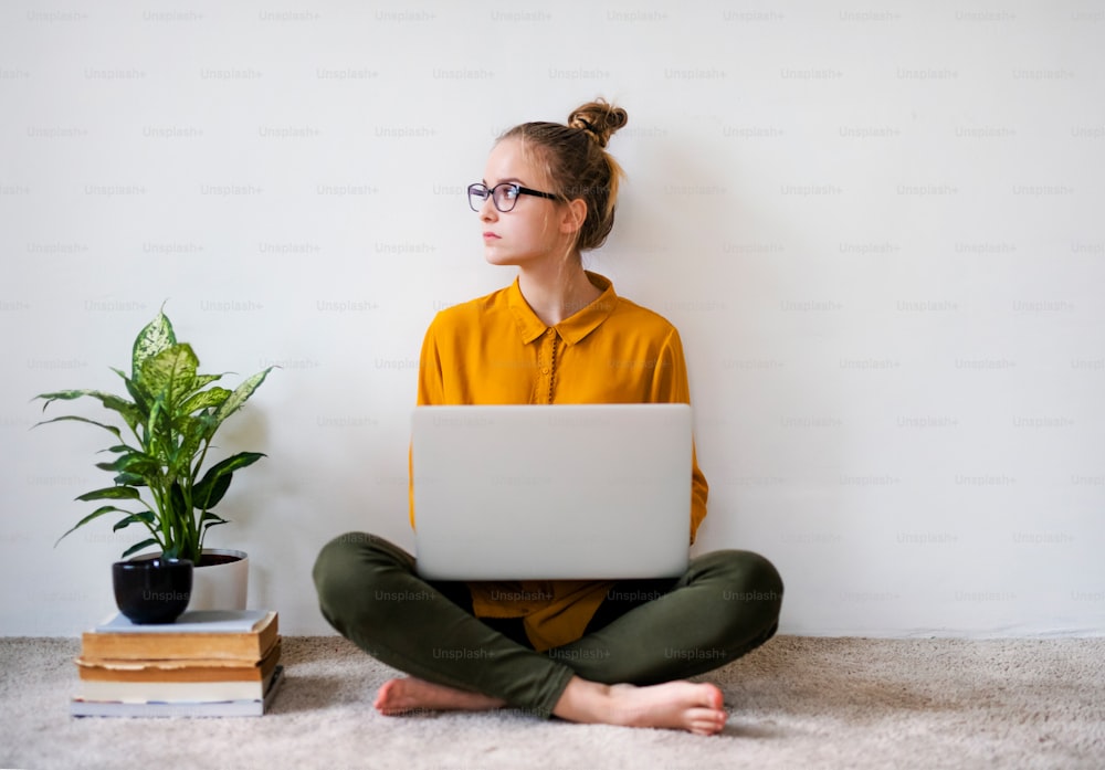 Uma jovem estudante universitária sentada no chão de casa, usando laptop ao estudar.