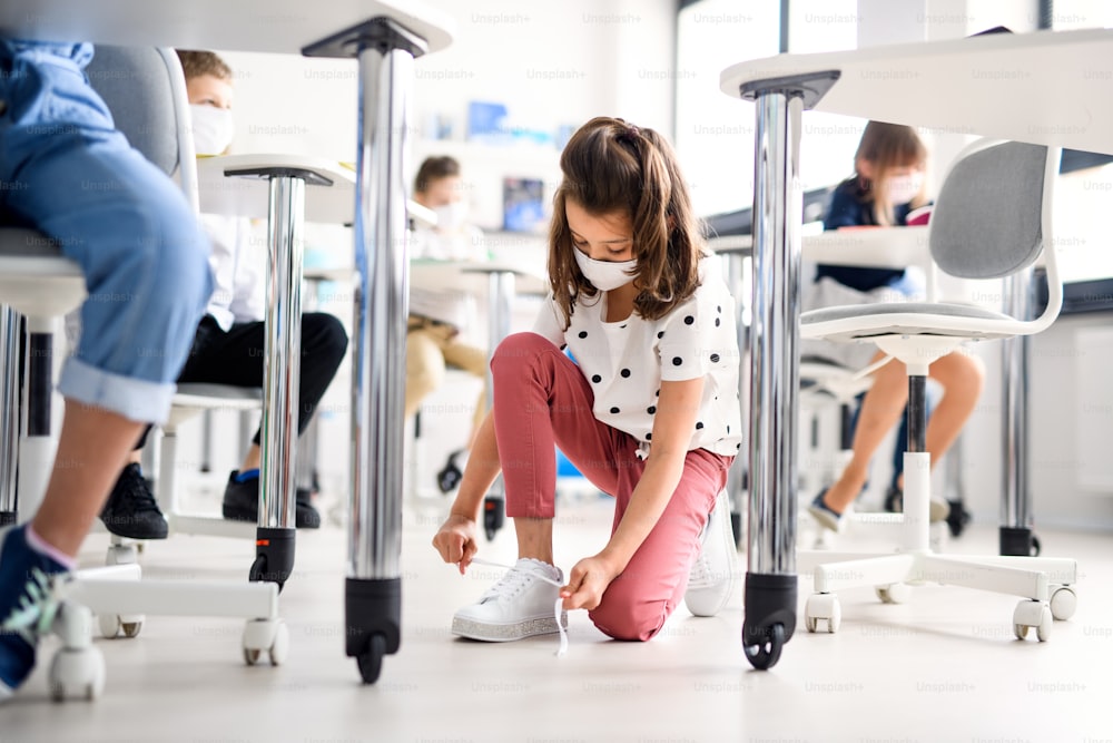 Child with face mask back at school after covid-19 quarantine and lockdown, tying shoelaces.