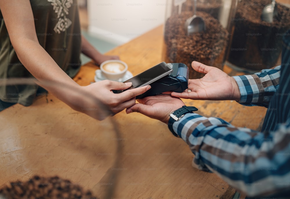 Kunden, die drahtlos oder kontaktlos mit Kreditkarte und NFC-Technologie bezahlen. Fokus auf die Hände