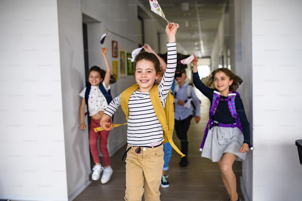 Group of cheerful children going home from school after covid-19 quarantine and lockdown, taking off face masks.