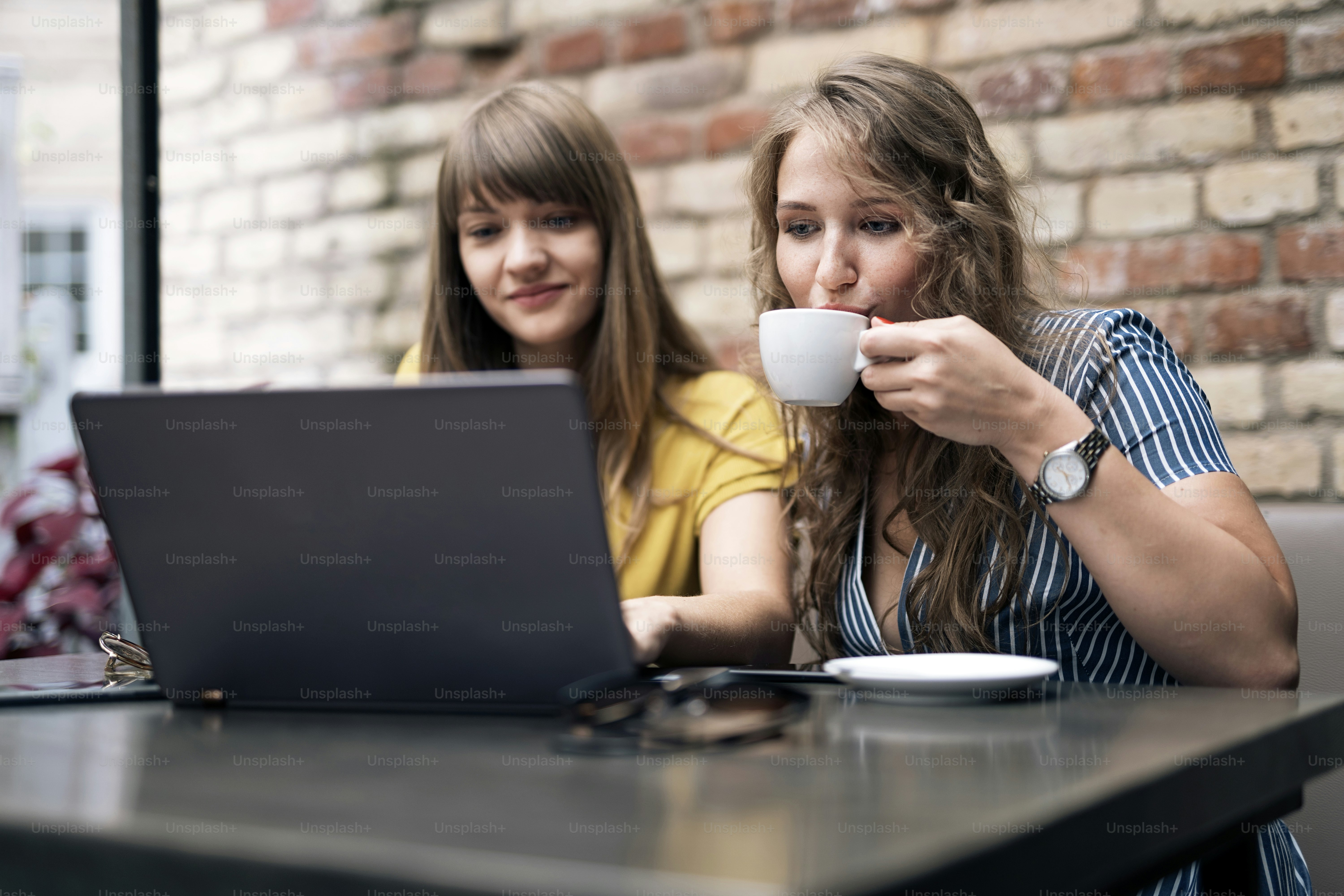Stylish young women having friendly meeting with cups of coffee while using the laptop