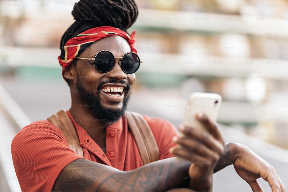 Foto de archivo de un atractivo chico afroamericano con rastas y un pañuelo usando su teléfono. Se está riendo.