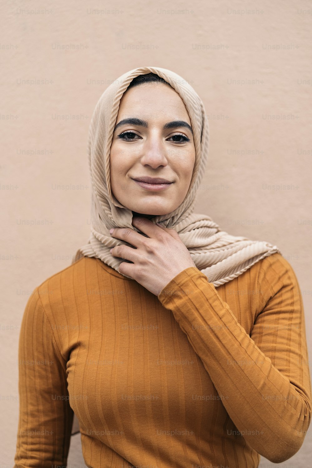 분홍색 머리 스카프를 두르고 웃으며 카메라를 바라보는 행복한 젊은 무슬림 여성.