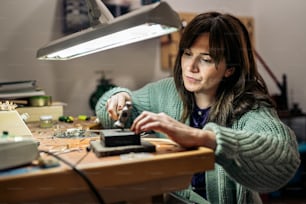 Stock photo of concentrated woman using hammer in jewelry workshop.