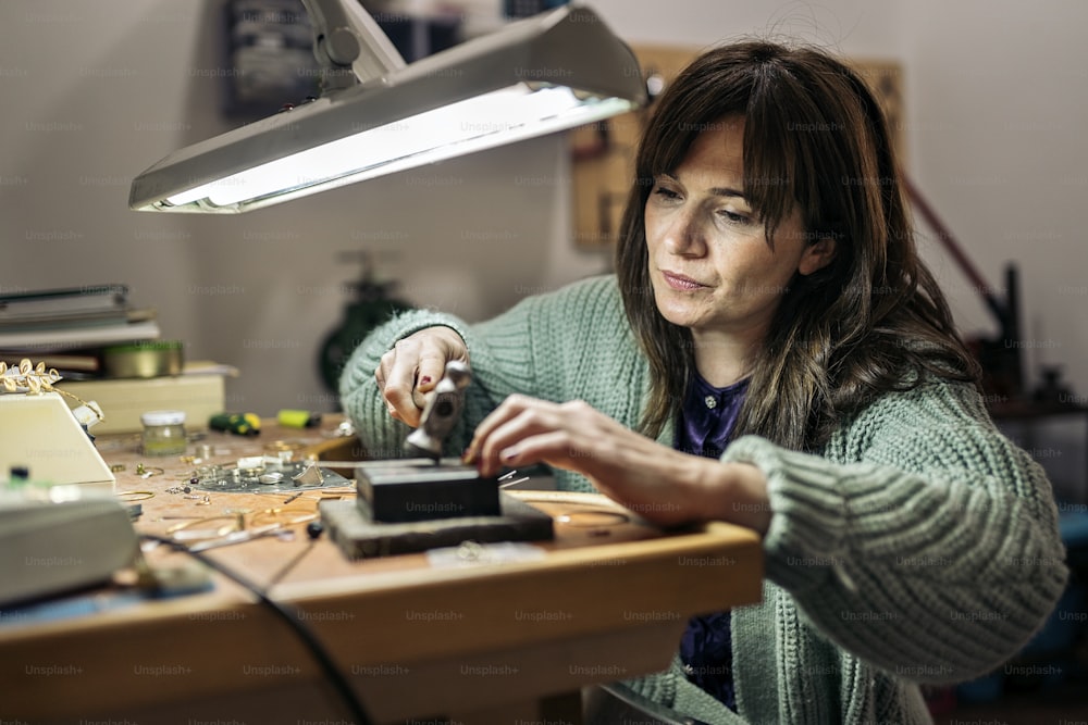 Archivio fotografico - donna concentrata usando martello in laboratorio di gioielli.