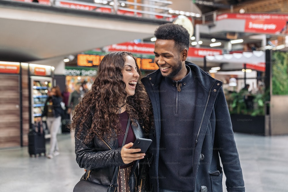 Stock photo of happy moment of interracial couple of lovers using phone in train station. They are in Madrid city.