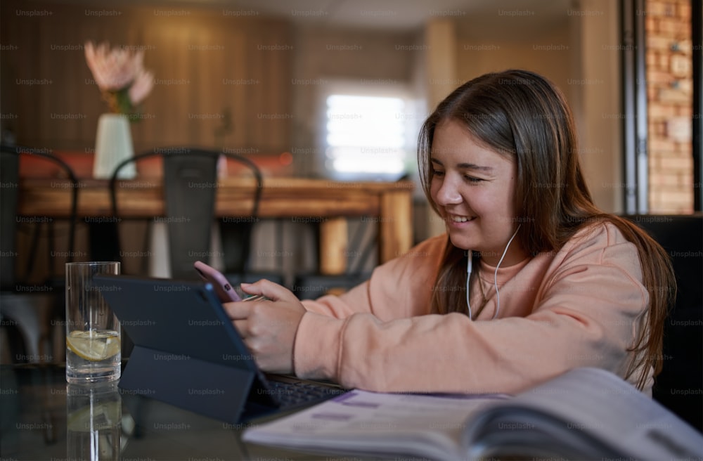 Retrato de una hermosa colegiala adolescente feliz y sonriente sentada en la mesa de café mensajeando, usando un teléfono inteligente en el interior moderno y acogedor de la sala de estar, estudiando y relajándose en casa. Educación en línea y concepto de elearning durante la cuarentena