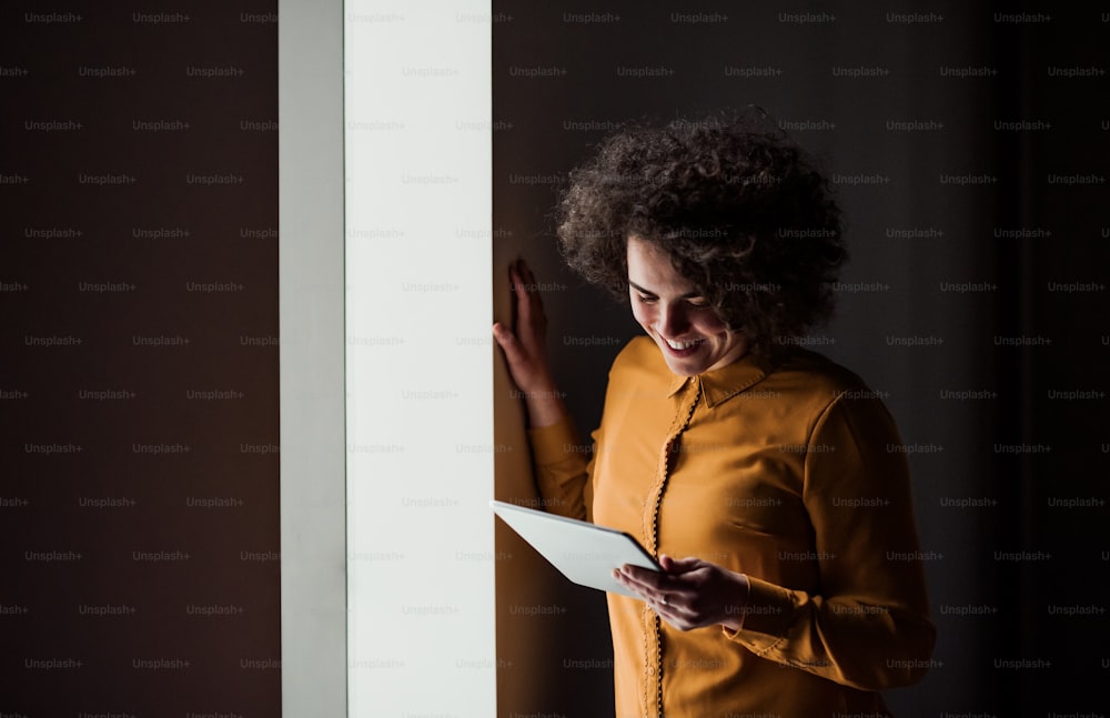 Retrato de una joven y alegre mujer de negocios con una tableta en el interior de una oficina. Espacio de copia.