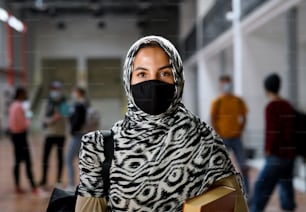 Estudiante islámico con mascarilla en el colegio o la universidad mirando a la cámara, concepto de coronavirus.