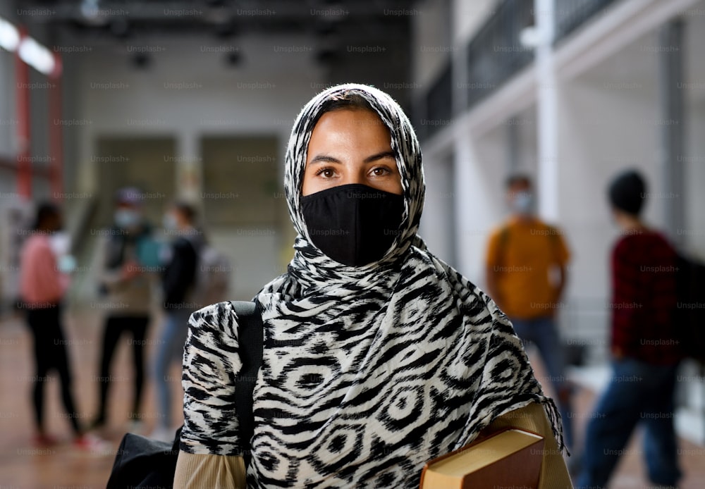 Studente islamico con maschera facciale al college o all'università guardando la macchina fotografica, concetto di coronavirus.