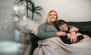 Young gay couple laying under a blanket holding each other , smiling and watching tv