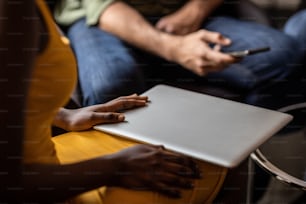 Primer plano de una empresaria africana sosteniendo una computadora portátil cerrada durante una reunión informal con colegas en una oficina