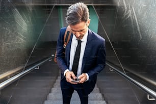 Hoher Winkel des selbstbewussten reifen männlichen Unternehmers im Anzug und mit Handy auf der Treppe der Unterführung stehend und konzentriert