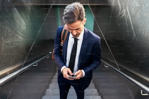 High angle of confident mature male entrepreneur in suit and with mobile phone standing on staircase of underpass and focused