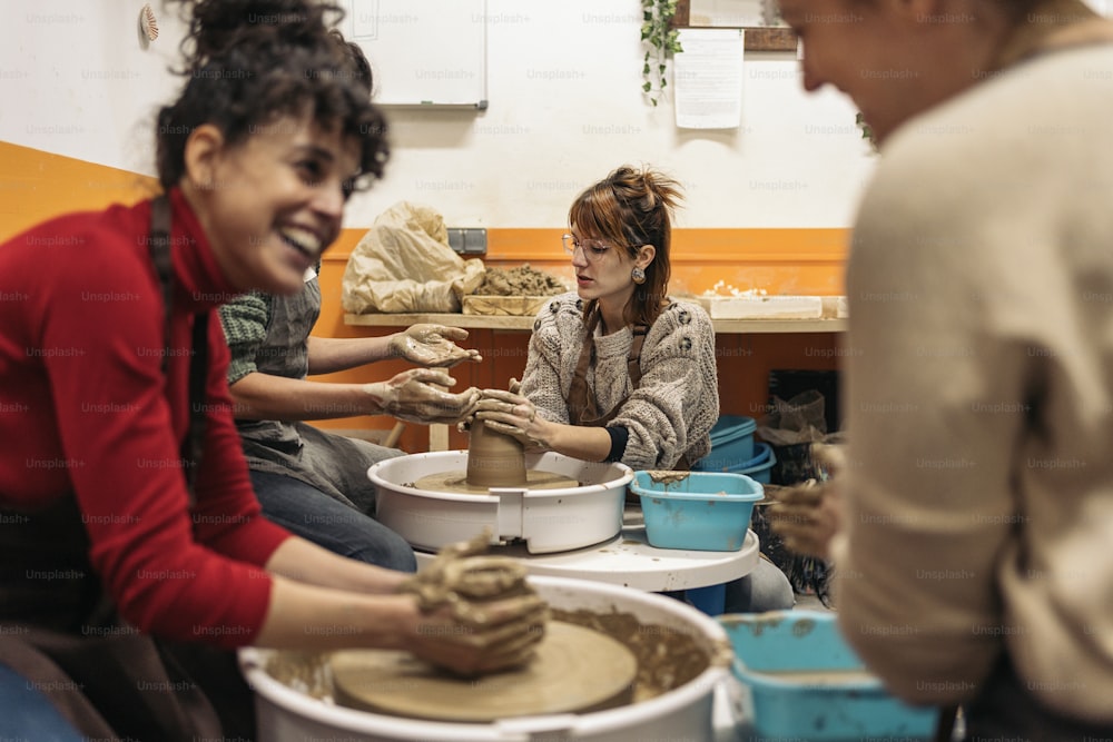 Stockfoto von glücklichen Frauen in Schürze, die hinter einer Töpferscheibe in einer Werkstatt arbeiten.