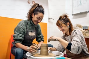 Stock photo of pottery teacher explaining to happy woman how to use spinning wheel.