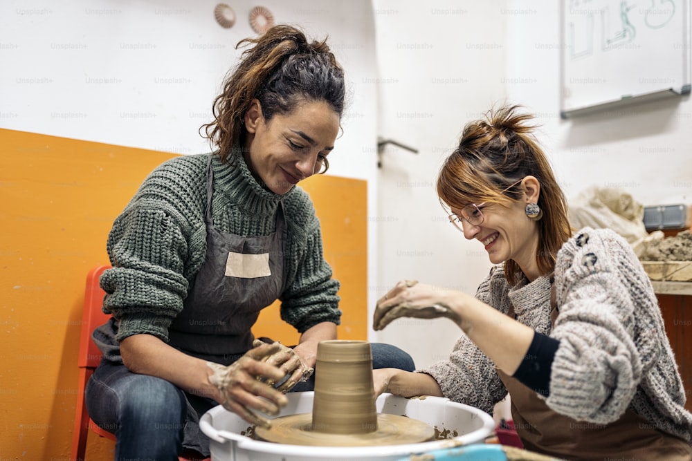 Foto de archivo de profesor de cerámica explicando a una mujer feliz cómo usar la rueca.