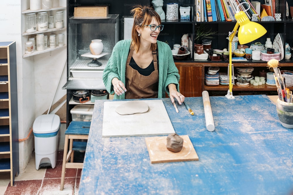 Foto de banco de imagens da mulher feliz no avental que trabalha no ateliê da cerâmica.