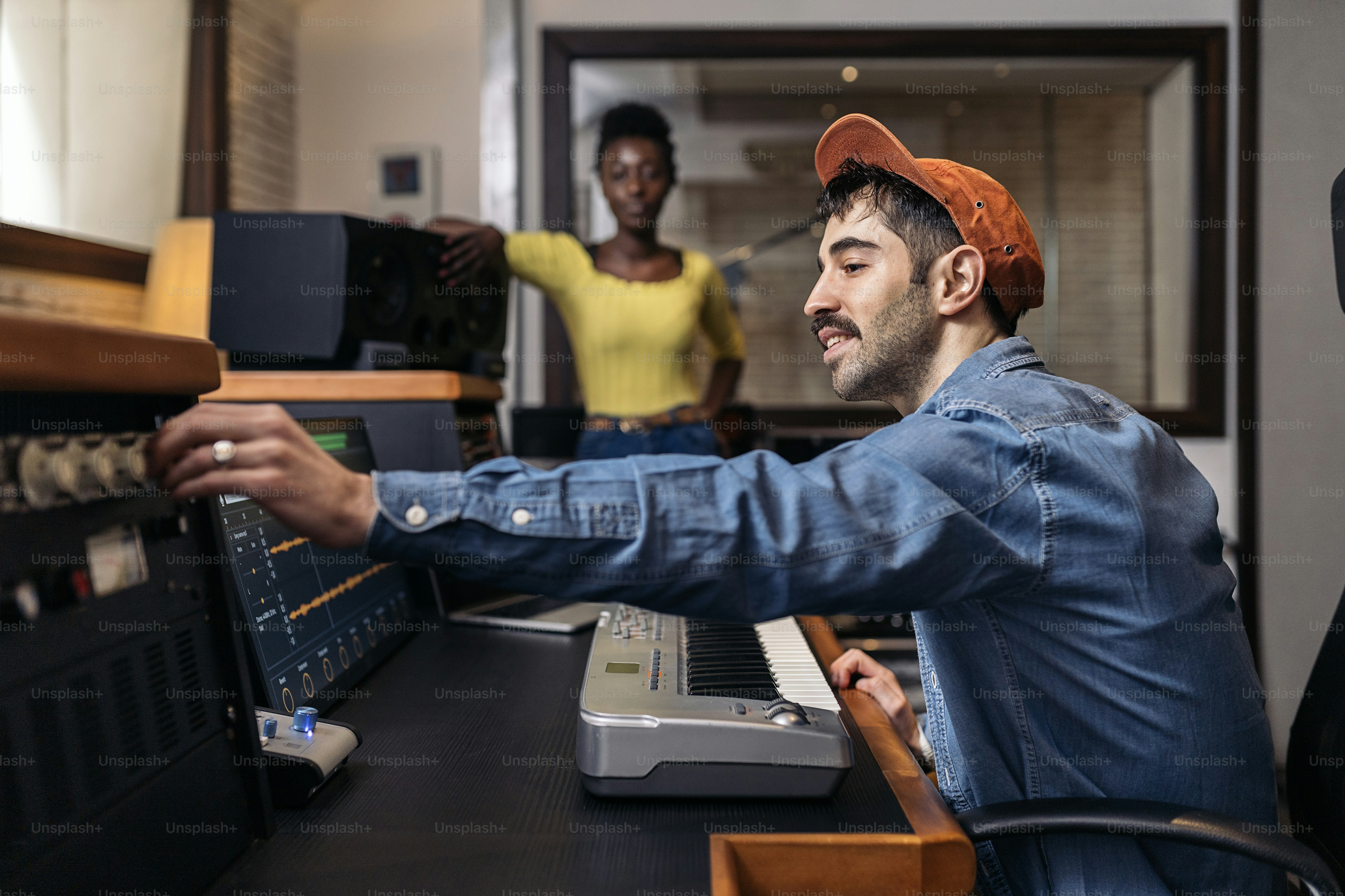 Stock photo of happy black woman in music studio and male producer using electronic piano keyboard.