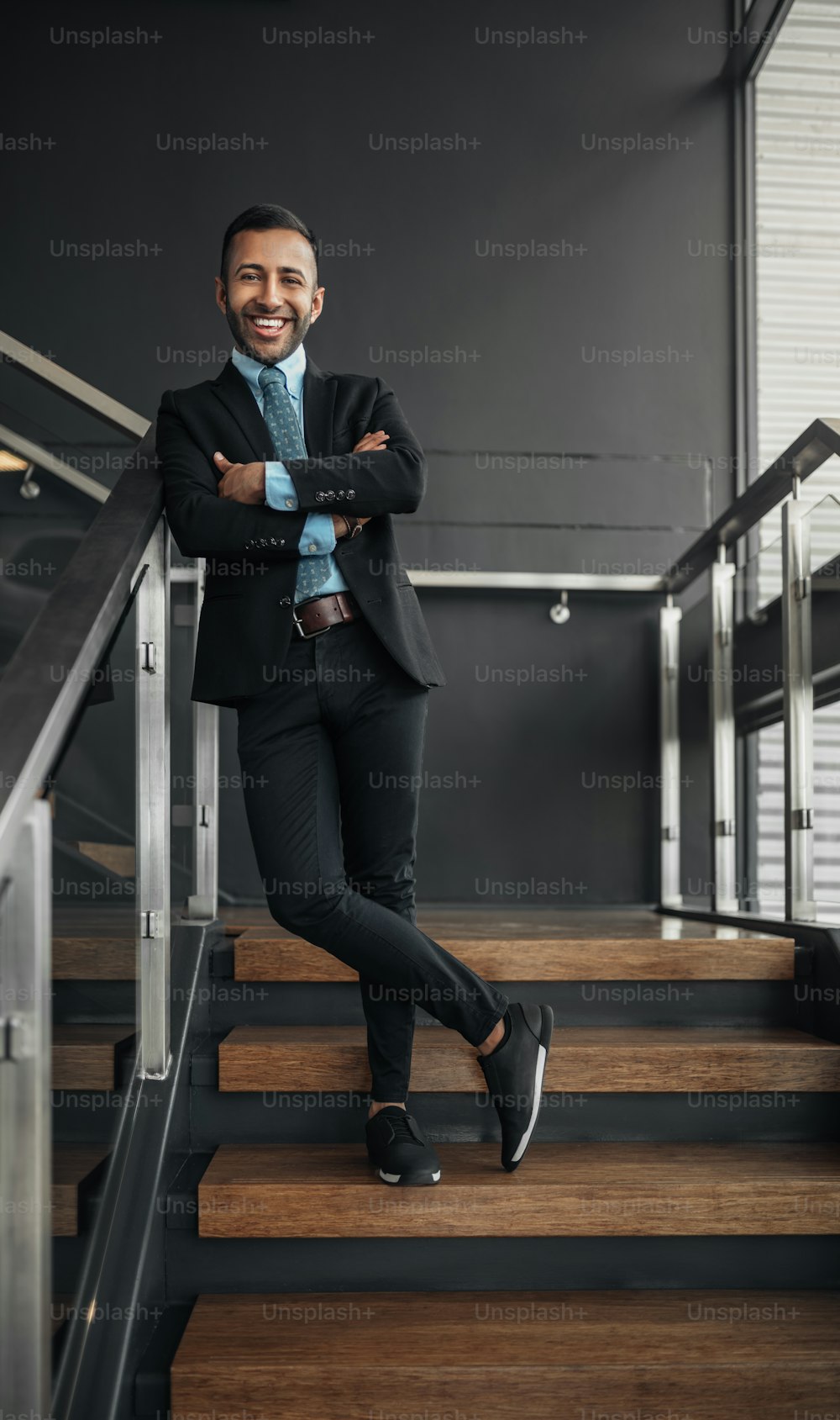 Erfolgreicher indischer, arabischer Geschäftsmann auf einer Treppe, lächelnd mit verschränkten Armen und Beinen