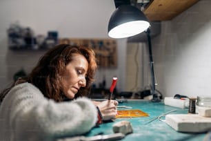 Concentrated adult woman working in jewelry workshop.
