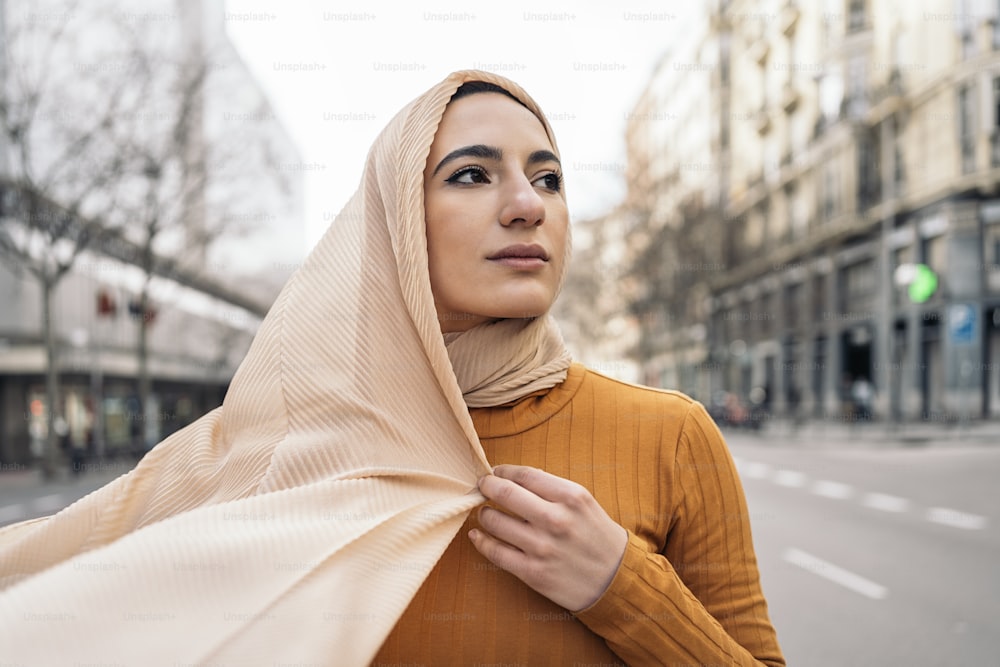 분홍색 머리 스카프를 두르고 웃으며 거리의 옆을 바라보는 예쁜 젊은 무슬림 여성.
