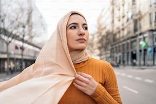 Pretty young muslim woman wearing pink head scarf smiling and looking to the side in the street.