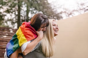 Happy proud lesbian couple having fun outdoors with gay flag