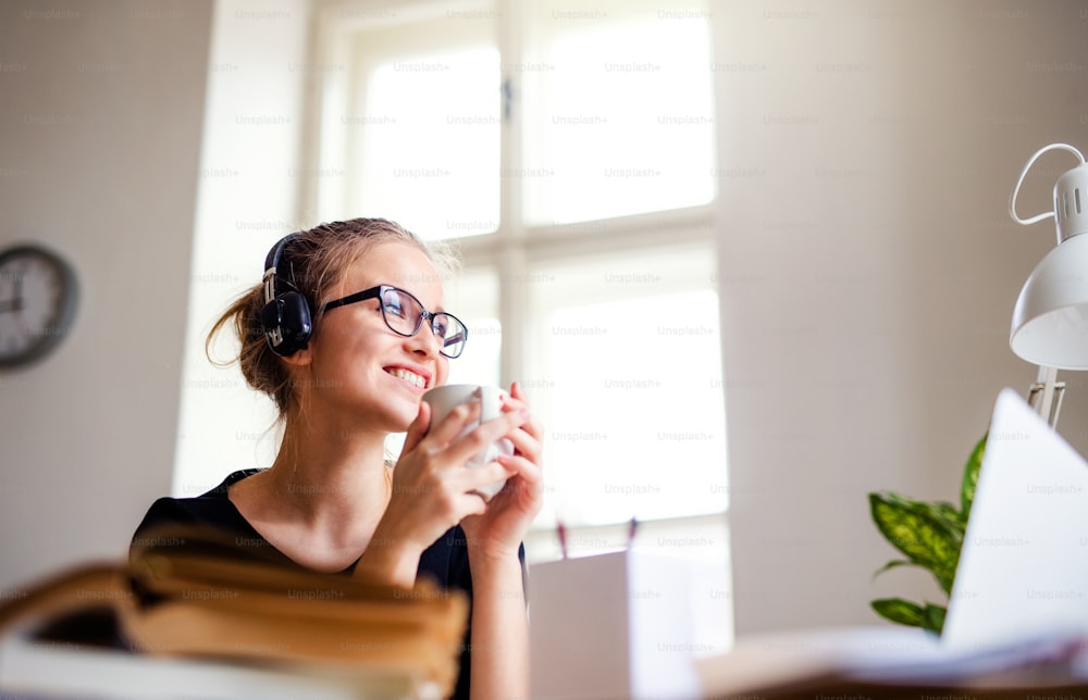 Una joven estudiante universitaria feliz sentada en la mesa de su casa, usando auriculares cuando estudia.