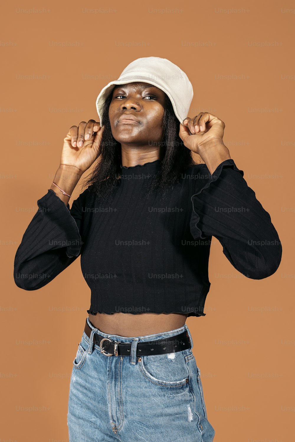 Stock photo of cool black girl wearing hat posing in studio shot against brown background.