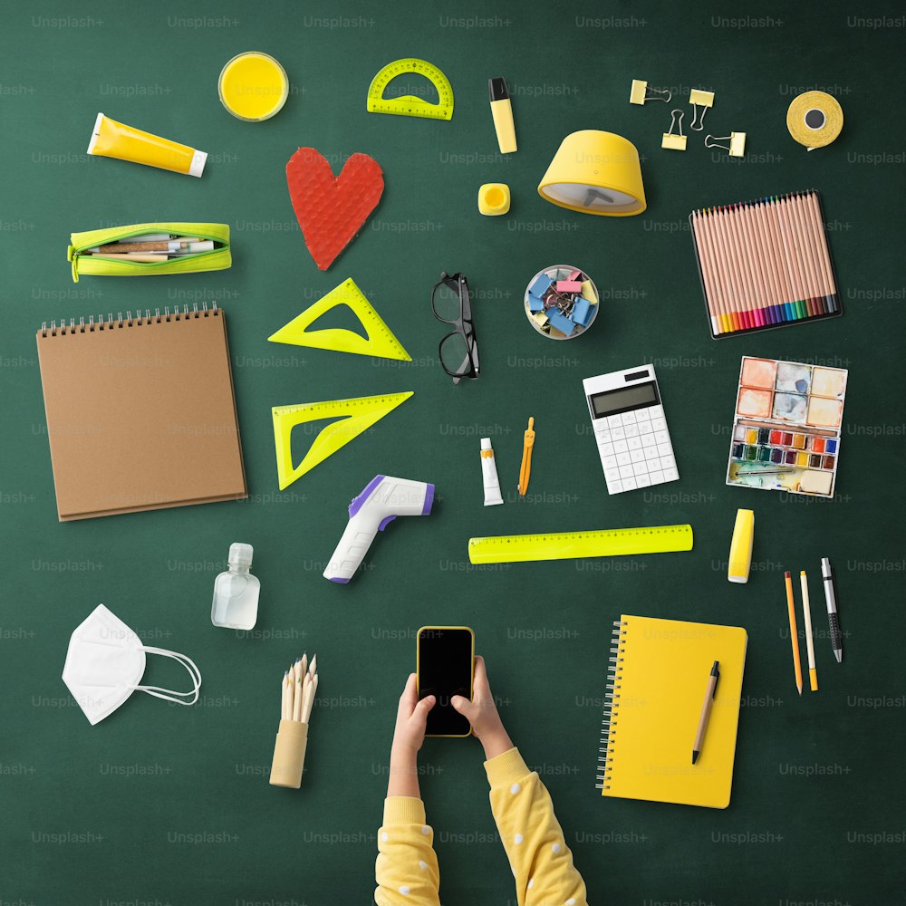 A flat lay top view of child with smartphone and school supplies, distance learning and coronavirus concept.