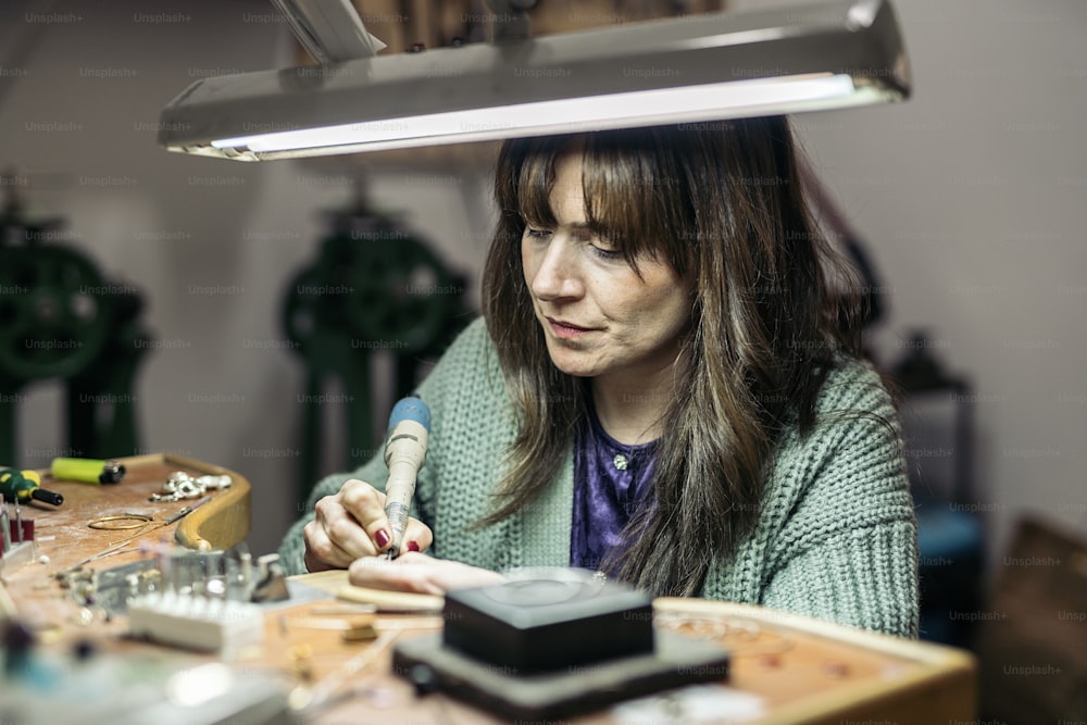 Donna adulta concentrata che lavora in un laboratorio di gioielli.