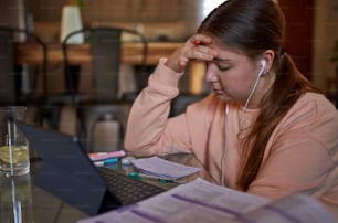 Portrait of young teenage school girl sitting at coffee table listening to music, using earphones in modern cozy living room interior, studying and relaxing at home. Online education and elearning concept during quarantine