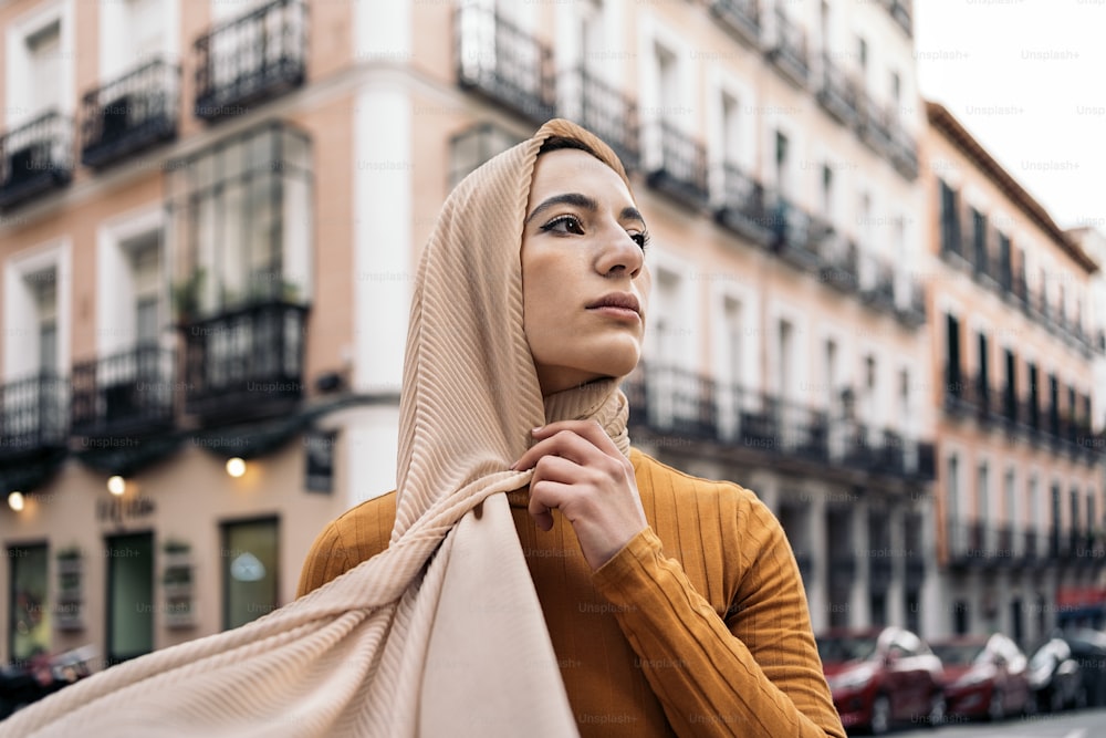 Beautiful young muslim woman standing in the street wearing hijab and looking at front.
