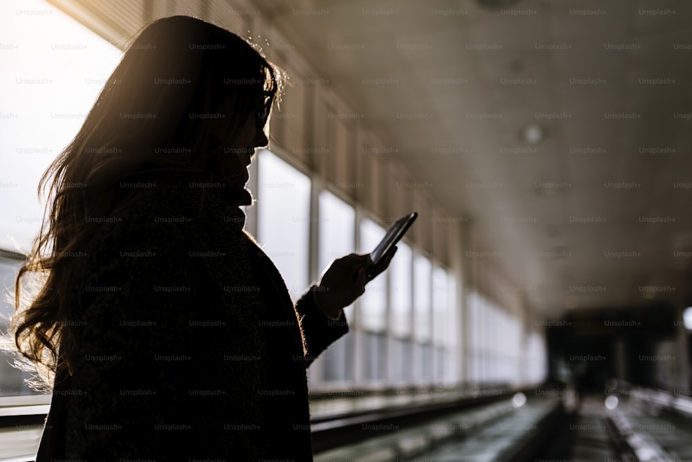 空港ターミナルで携帯電話を使用している見分けのつかない女性。空港のコンセプト。