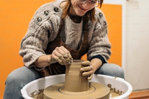 Stockfoto einer konzentrierten Frau in Schürze, die hinter einer Töpferscheibe in einer Werkstatt arbeitet.