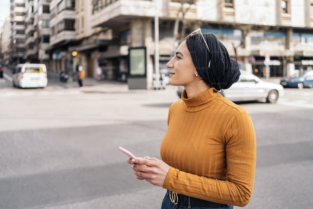 頭にスカーフをかぶったかなり若いイスラム教徒の女性が、通りで携帯電話を使い、横を向いています。