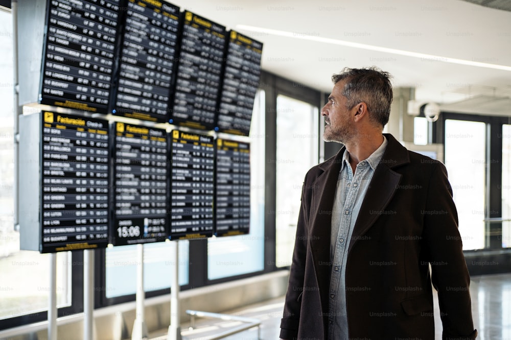空港で出発時刻表を見ている白人のビジネスマンのストックフォト。彼はスーツケースを持っています。普段着で着ている。
